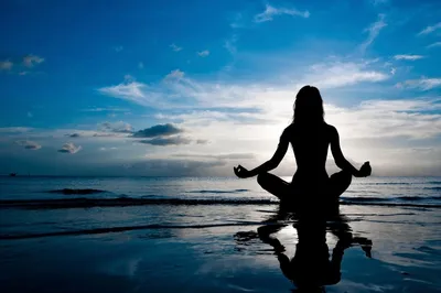 "Silhouette of a woman meditating on a beach at sunrise, reflecting peace and mindfulness."